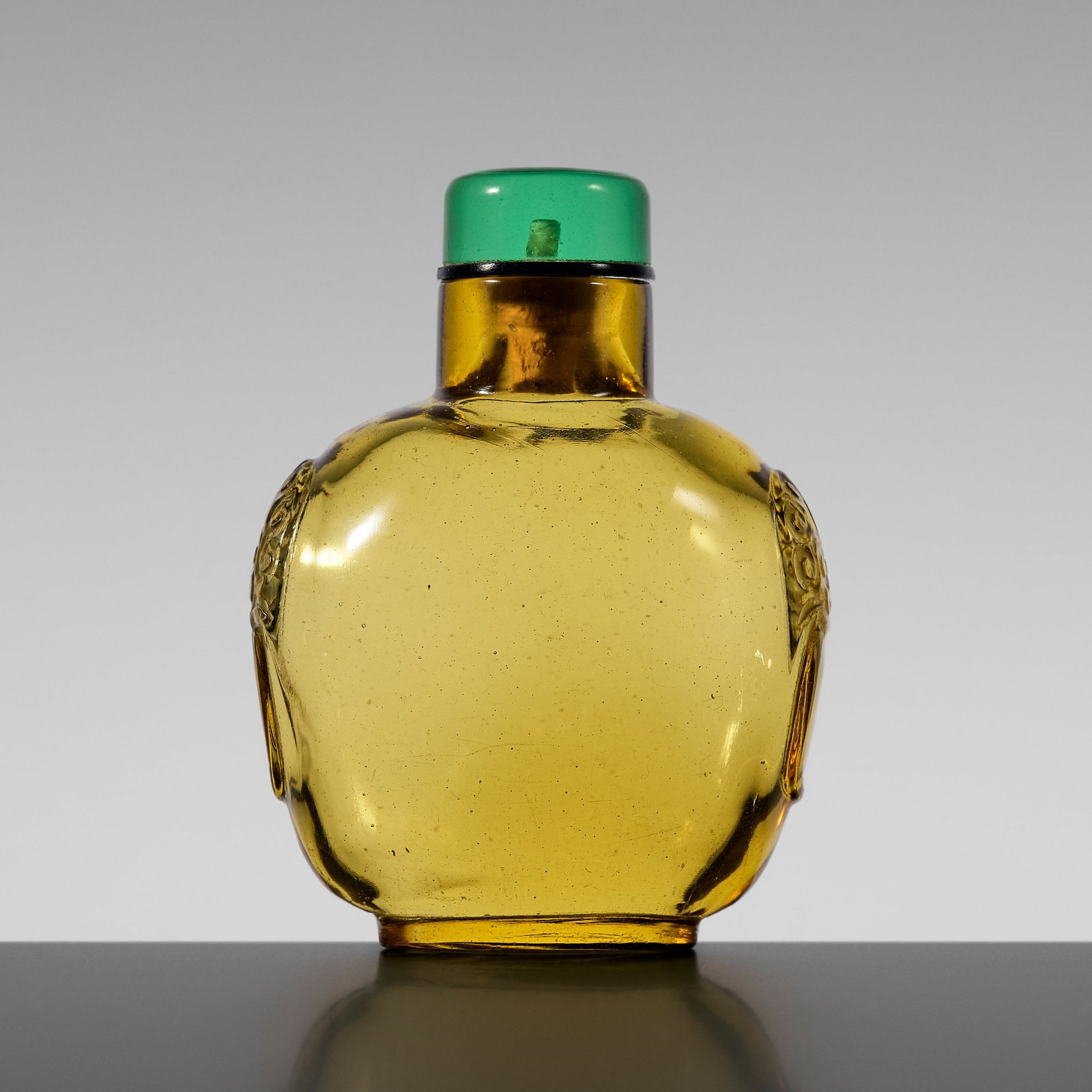 AN AMBER-YELLOW GLASS SNUFF BOTTLE, 18TH CENTURY: AN AMBER-YELLOW GLASS SNUFF BOTTLE, 18TH CENTURY China. Of square form with rounded corners, supported on an oval foot and rising to a cylindrical neck with subtle concave lip, the narrow sides flanke