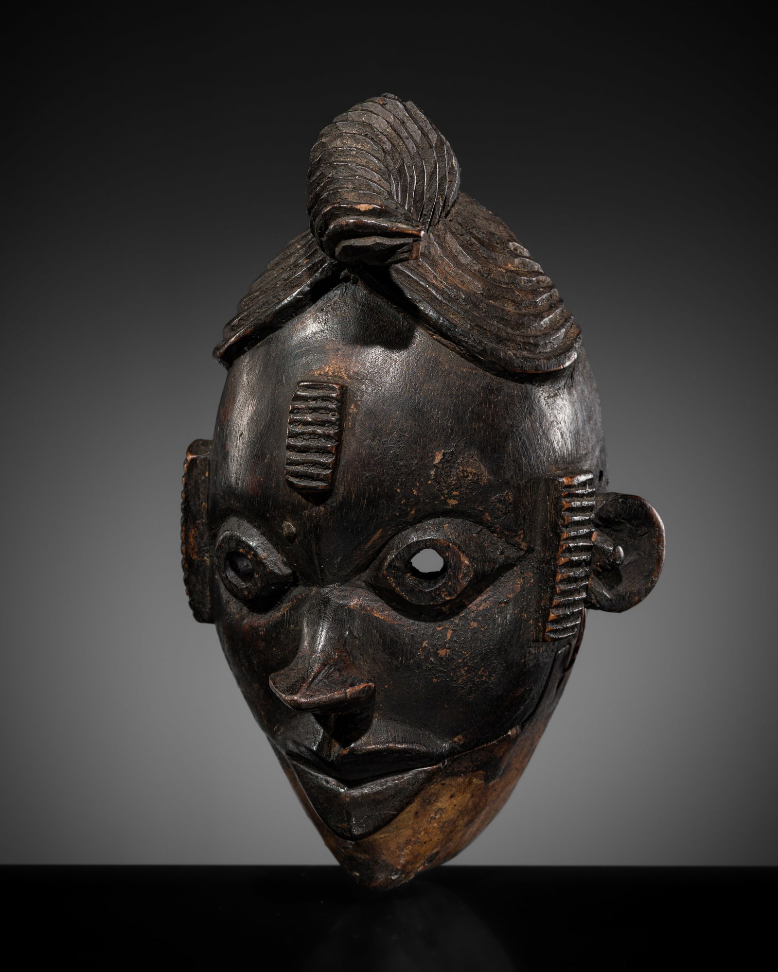 AN OGONI WOOD MASK, 19TH-20TH CENTURY: AN OGONI WOOD MASK, 19TH-20TH CENTURY This lot is from a single owner collection and is therefore offered without reserve Boldly carved of oval form with a pointed chin, the face with almond-shaped pi