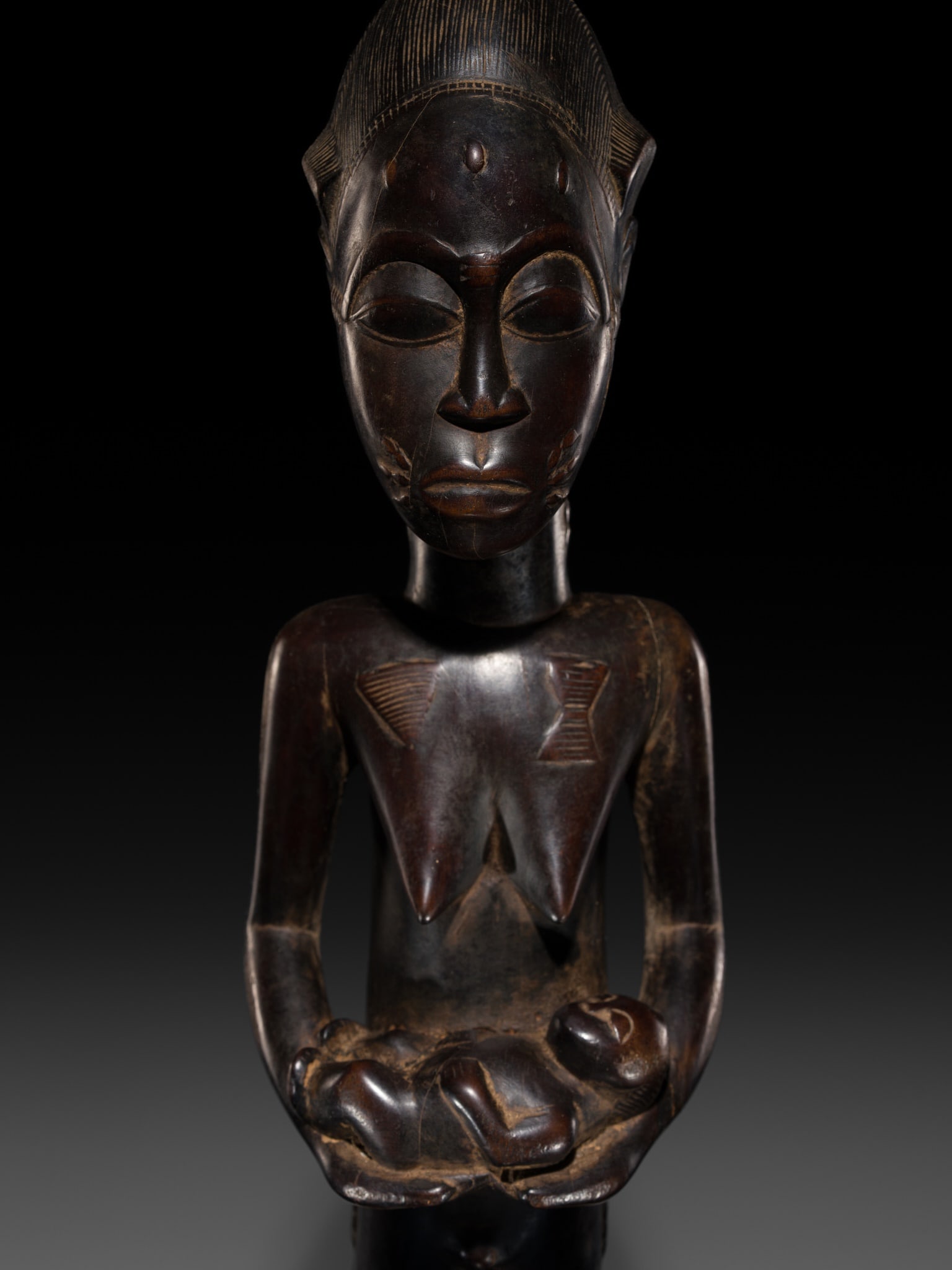 A BAULE WOOD MATERNITY FIGURE, LATE 19TH TO MID-20TH CENTURY: A BAULE WOOD MATERNITY FIGURE, LATE 19TH TO MID-20TH CENTURY This lot is from a single owner collection and is therefore offered without reserve Côte d'Ivoire. Finely carved seated on a chair, ho