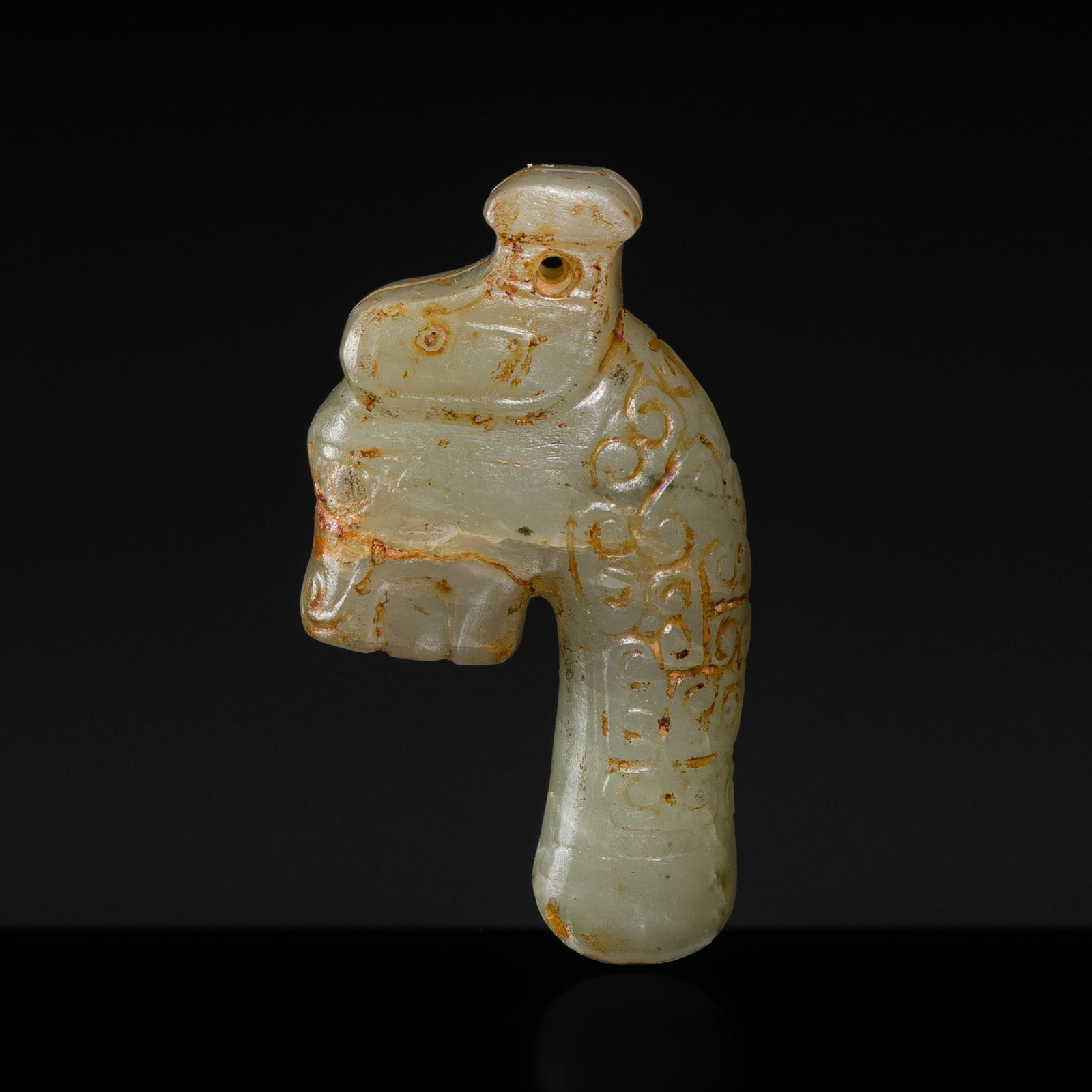 A RARE PALE CELADON 'DRAGON HEAD' PENDANT, LATE SHANG TO WESTERN ZHOU DYNASTY: A RARE PALE CELADON 'DRAGON HEAD' PENDANT, LATE SHANG TO WESTERN ZHOU DYNASTY China, c. 1050-770 BC. Skillfully carved, set atop a slender, gently waisted neck decorated with tight C-shaped scrollwork