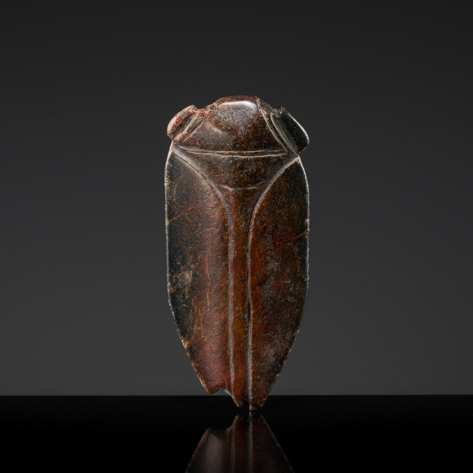 A DARK BROWN JADE TONGUE AMULET IN THE FORM OF A CICADA, HAN DYNASTY: A DARK BROWN JADE TONGUE AMULET IN THE FORM OF A CICADA, HAN DYNASTY China, 206 BC-AD 220. Of flattened form, skillfully carved as a stylized cicada with projecting eyes and elongated wings folded clo