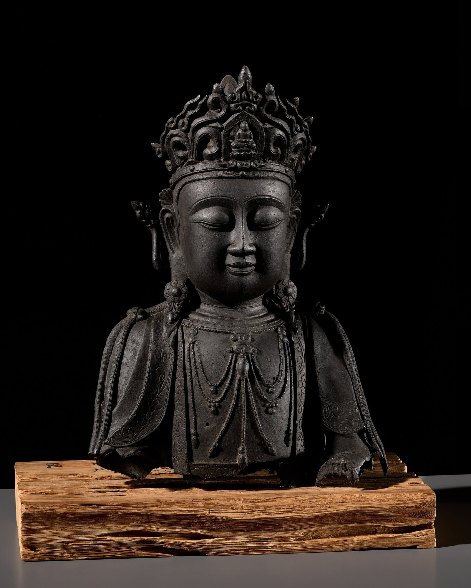 A MONUMENTAL BRONZE BUST OF GUANYIN, MING DYNASTY, MOUNTED ON A SACRED KASUGA CEDAR WOOD STAND BY: A MONUMENTAL BRONZE BUST OF GUANYIN, MING DYNASTY, MOUNTED ON A SACRED KASUGA CEDAR WOOD STAND BY SUIREI Expert's note This bronze bust of Guanyin once belonged to an exceptionally large figure for th