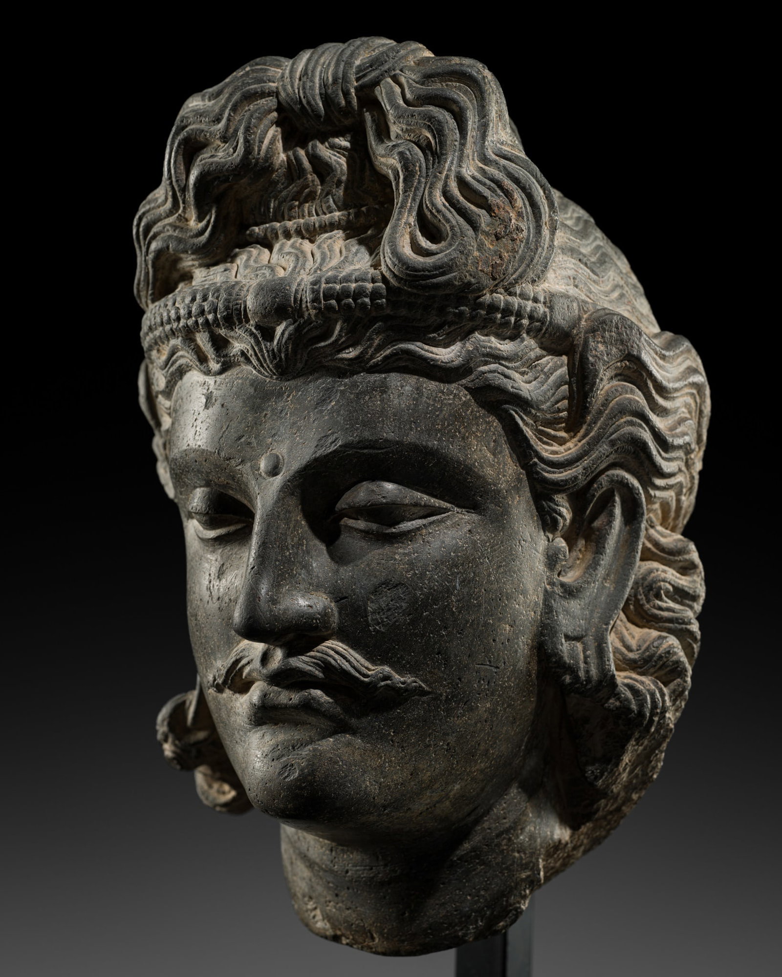 A LARGE SCHIST HEAD OF MAITREYA, ANCIENT REGION OF GANDHARA, 2ND-3RD CENTURY: A LARGE SCHIST HEAD OF MAITREYA, ANCIENT REGION OF GANDHARA, 2ND-3RD CENTURY Kushan period. The oval face with heavy-lidded almond-shaped eyes articulated by broad arching eyebrows, a curling mustache