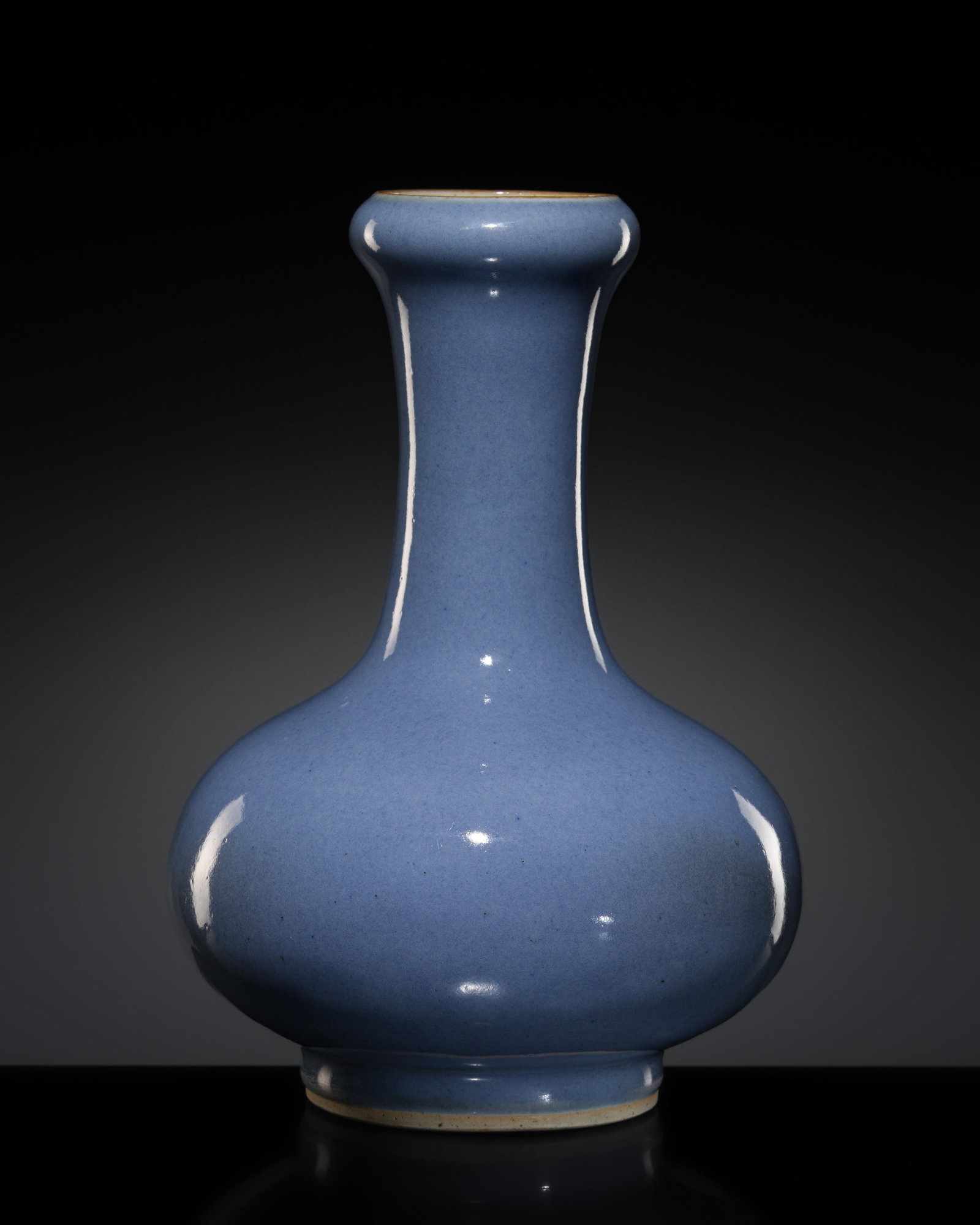 A PALE LAVENDER-BLUE-GLAZED BOTTLE VASE, 18TH CENTURY: A PALE LAVENDER-BLUE-GLAZED BOTTLE VASE, 18TH CENTURY China. The bulbous body rising from a circular foot to a tall cylindrical neck surmounted by a broad garlic-shaped mouth, the exterior covered ove