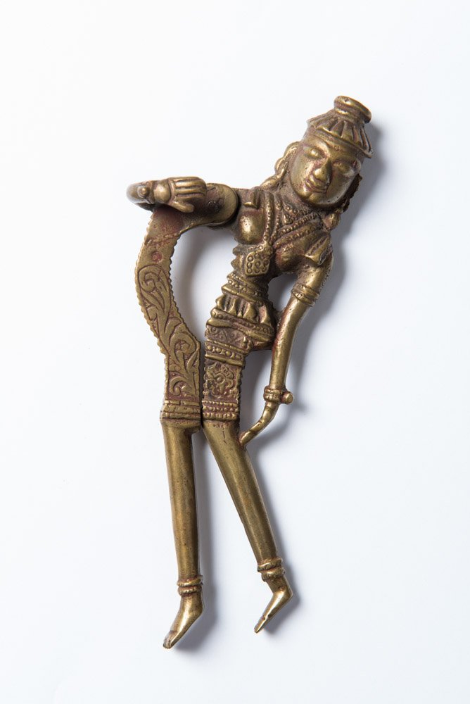 BETEL NUT CRACKER: Yellow bronze. Asia, China, ca. 19th century HEIGHT 18,8 CM From an Austrian private collection Unusual figural betel nut cracker, rendered as a female devi with long legs, richly bejeweled and in dan