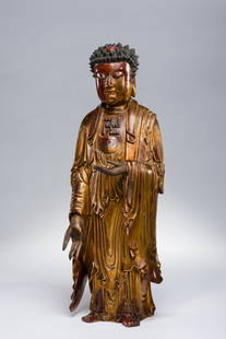 WOOD FIGURE OF STANDING BUDDHA: Wood, lacquer, gilding. China, Qing Dynasty, 18th – 19th centuryVery fine craftsmanship, depicting Buddha clad in a floor long robe falling with rich pleats, one hand hanging flank in the varadra