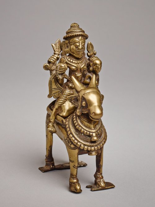 SHIVA WITH UMA ON A BULL: Yellow bronze. India, Maharashtra, 17th to 18th cent. One of a two-part bronze, interesting and compactly designed, with a four-armed Shiva holding a trident, axe and string-of-pearls in his hands. Hi