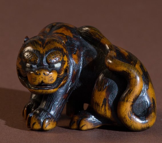 MASATOMO: TIGER: Netsuke, wood and horn. Japan, 19th cent. Very well-worked tiger, whose wildness comes through at best. The sleek feline predator is rendered dense and well-rounded. The fur pattern is unusual, here c