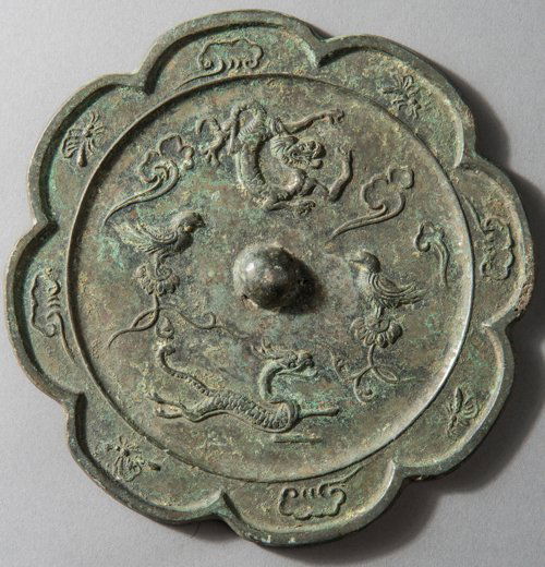 MIRROR OF BLOSSOM FORM WITH BEASTS: Bronze. China, in the style of Tang Dynasty The center knob with loop is of eight-lobed form in the kind of a flower, encircled by a relief of four animals (fiery dragon, scaled horned Qilin running a