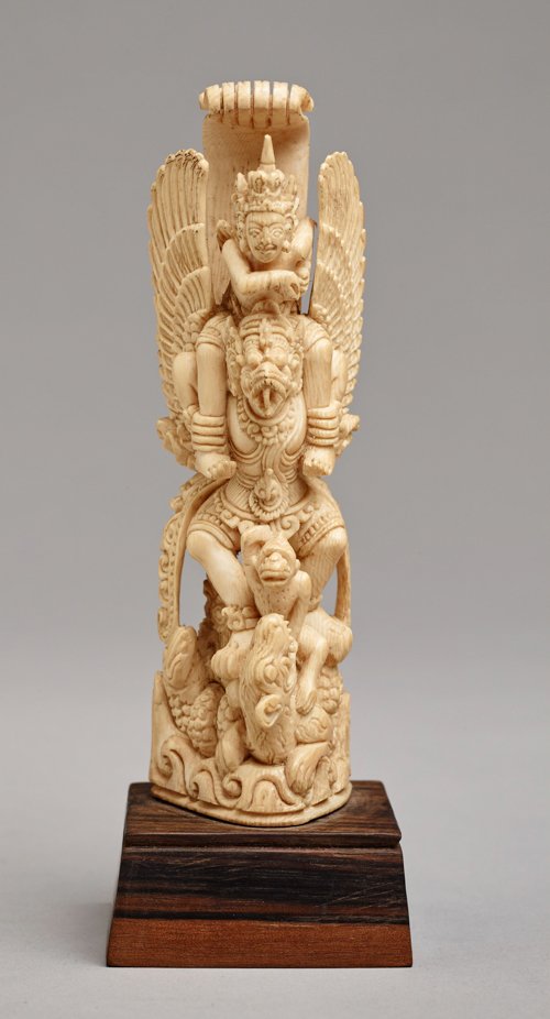 THE SEMI GOD BIRD GARUDA: Ivory. Indonesia, late 19th to 20th cent. Detailed multi-figured scene focusing on Garuda, the semi god bird with an expressive head in the typical Indonesian style and human body. He is holding a sit