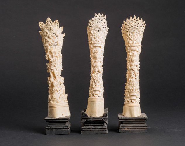 THREE FIGURATIVE ORNAMENTAL CARVINGS: Ivory. Indonesia, 19th - 20th cent. Two are executed very similarly with a kind of open-worked crowning over the expressive mask of a mythical creature, repeated in the lower area. In between is the d