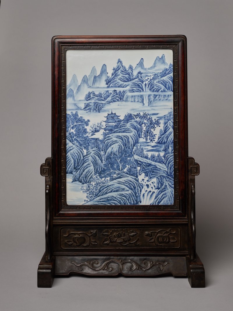 PORCELAIN PICTURE WITH MOUNTAIN LANDSCAPE: Porcelain with blue underglaze. China, late Qing, 19th cent. The picture is massively framed and rests on a stand with legs. Cobalt blue painting under the glaze offers a romantic landscape with rocks