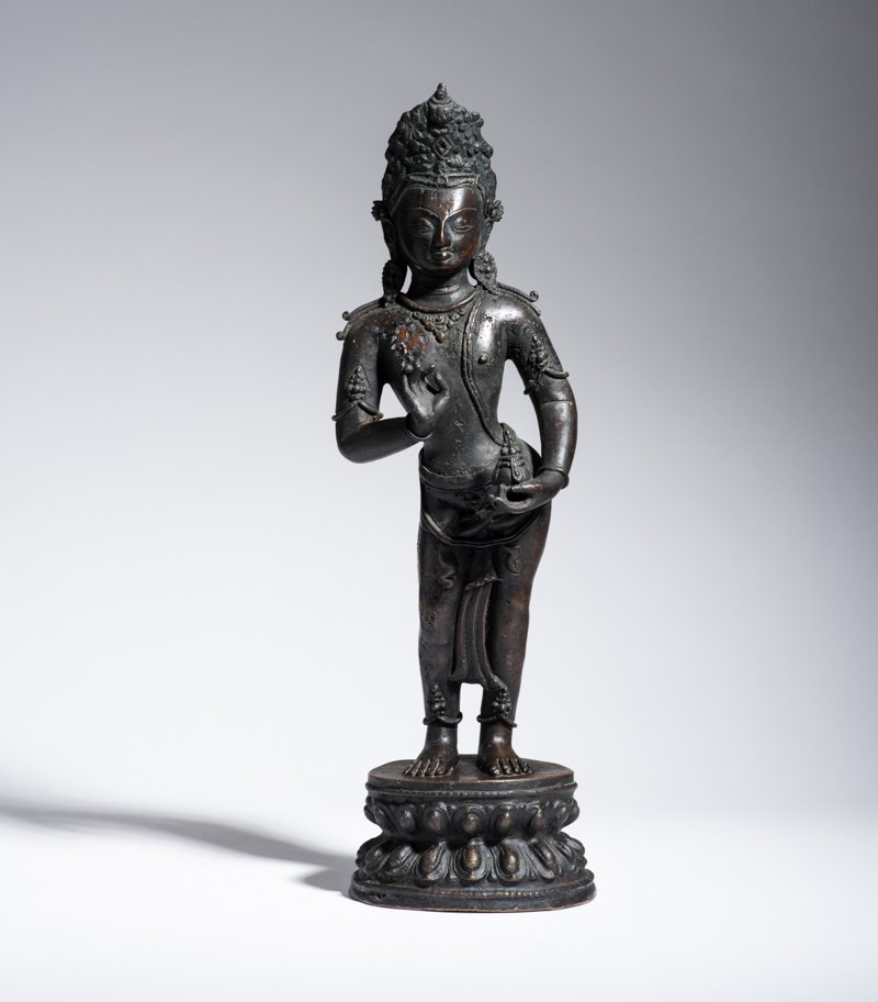 BODHISATTVA AVALOKITESHVARA WITH NECTAR VASE: Bronze. Nepal, 19th to 20th cent. A bodhisattva Avalokiteshvara with a tall crown, standing on a round lotus pedestal. The elegant tribhanga pose with exposed hip is striking, while the chest offers m