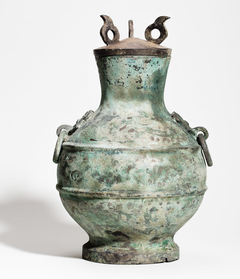 ARCHAIC BRONZE VESSEL WITH LID: Bronze, silver. China, Western Han Dynasty (206 BC to turn of the eras) A once very magnificent vessel of the Hu type with spherical, ribbed body, the neck funnel-shaped with flush rim. Two notable ta