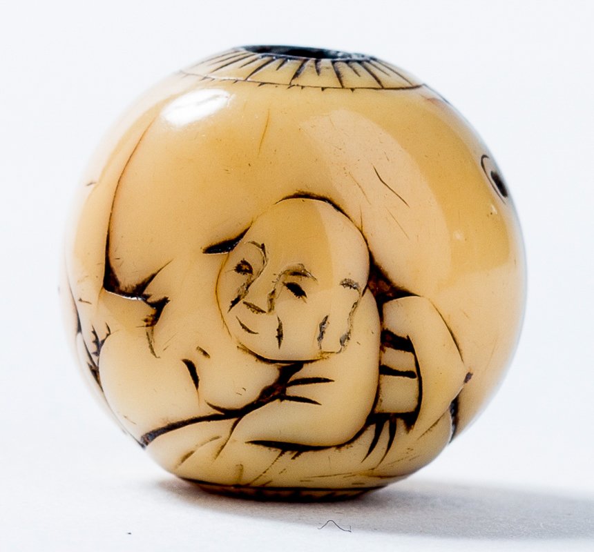 RECLINING MAN: Ojime, ivory. Japan, 19th cent. Spherical ojime with kiku-rosetted channel openings. A lying man is depicted in soft relief, whereby a spooky big hand is grabbing toward his lower body (medicinal, ero