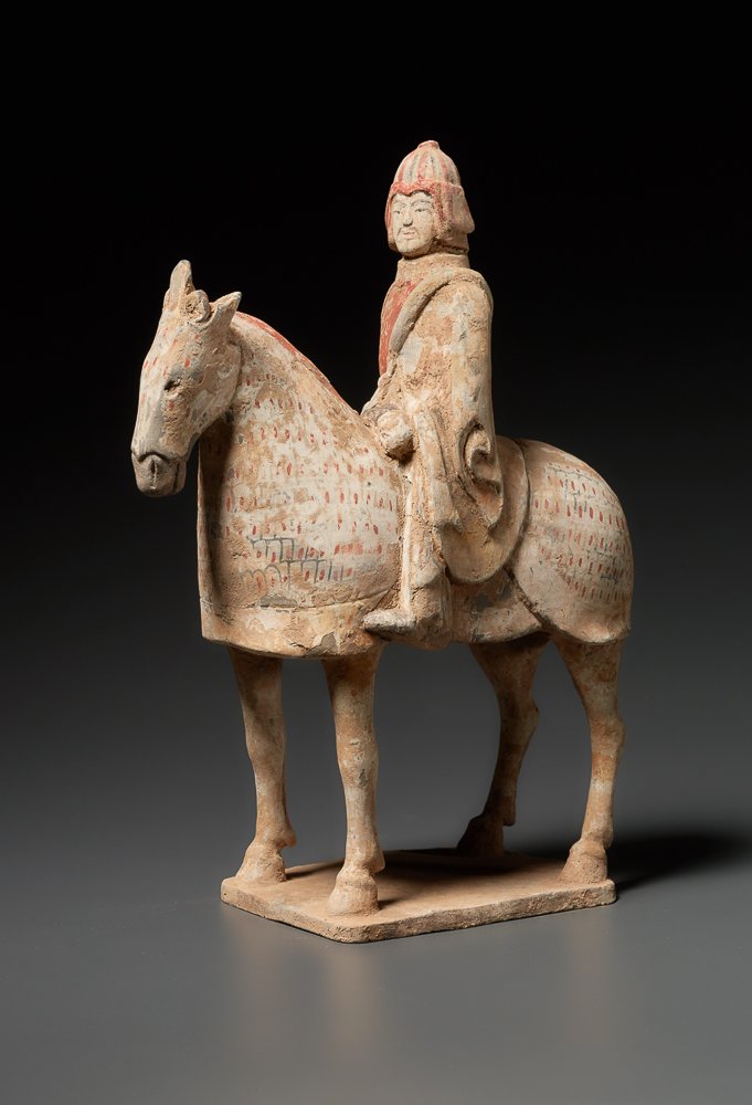 EQUESTRIAN WARRIOR: Terracotta with painting. China, Wei Dynasty (5th to 6th cent.) Standing horse in armor on a rectangular plate. The steed´s harness is composed of many parts; also the head has armor and the indi