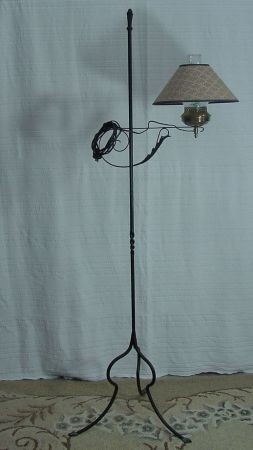 Black Iron Floor Lamp: Almost appears to be blacksmith made iron floor lamp, 3 Legged, Footed, With Twisted Shaft. Electric And In Working Order. Brass Oil Lamp Type Burner With Glass Chimney. 61 3/4" Tall.
