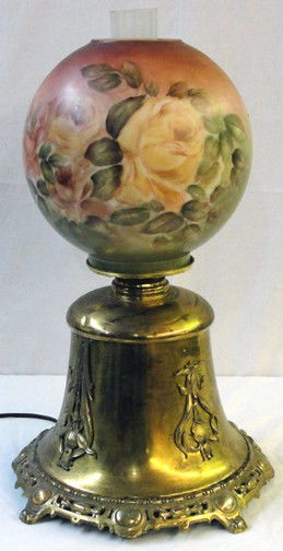 A Brass Bell Shaped Victorian Table Lamp: Ornate brass base with applied brass decorative blossoms, bell shaped brass frame, hand painted roses ball shade. The lamp originally was kerosene and has been drilled for electrification and is now i