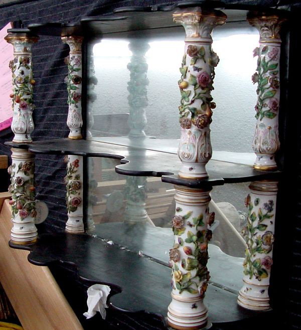 A Meissen/Dresden Style Porcelain Shelf: Dresden/Meissen wall shelf, 19th century hanging wall shelf in ebonized wood with scalloped shelves, mirrored back, porcelain flowers on front columns, either lady bugs and bees darting around the flo