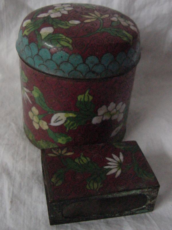 A Chinese Cloisonne Round Box & Match Holder: Marked China, clay red background with matching white floral and leaf designs, probably 1920s era, small nicks to edge of the lid of the cigarette box, an old match box with strikers on the side openi