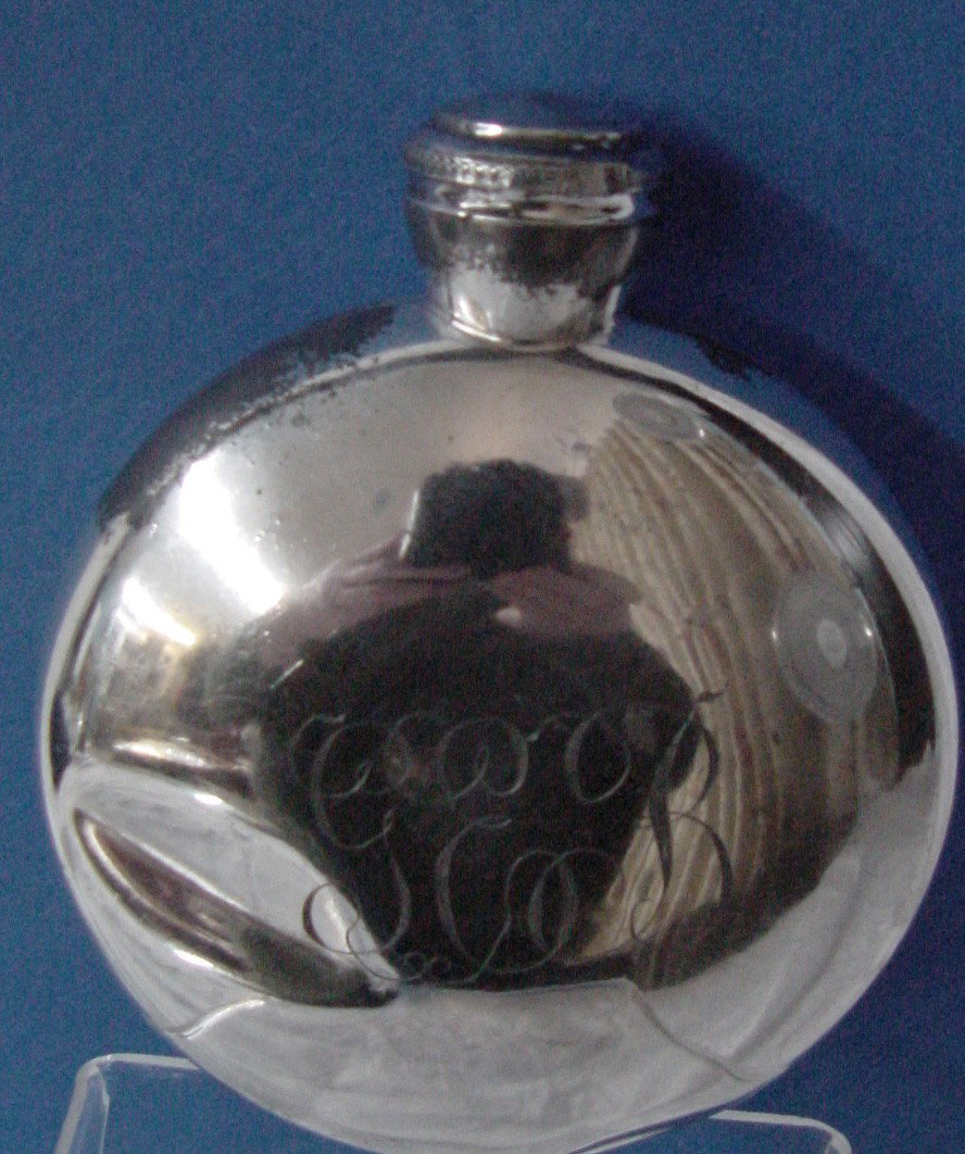 A Early 20th Cent. Flask Silver Plated: Pretty old monogram of GEB, silver plated with some plate coming off, looks as if holds about a half pint, easily placed in a pocket for use, minor dents from use, 4" wide by 3/4" thick with a shaped 