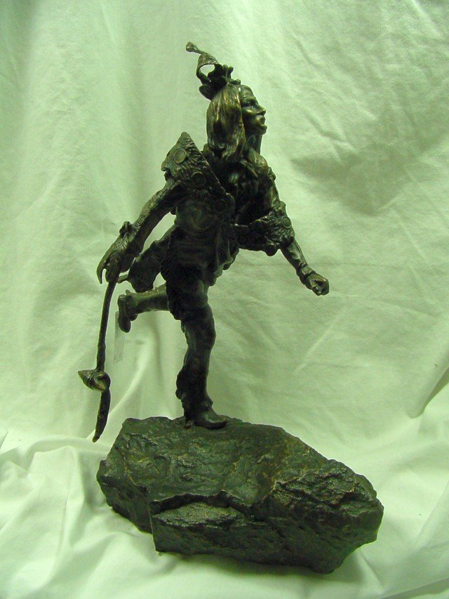 Carl Kauba Indian Bronze: Signed on the base C Kauba, standing 13 1/2" tall, 9" deep or wide, an Indian is standing on his right leg, holding a club and draped in some sort of stylized band or shawl with feathers. The original