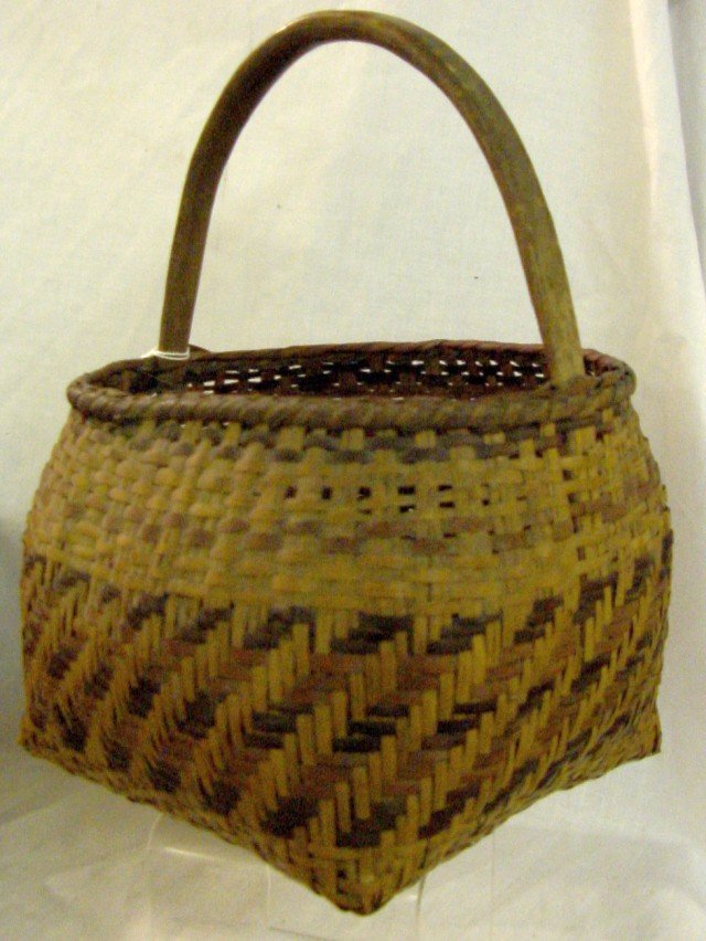 Cherokee River Cane Basket w/Handle: Likely to be by Rowena Bradley, 1960s, earlier design and coloration, triple woven rib extending up from a herringbone base, walnut and bloodroot dyes with river cane, notched wooden arched handle. On