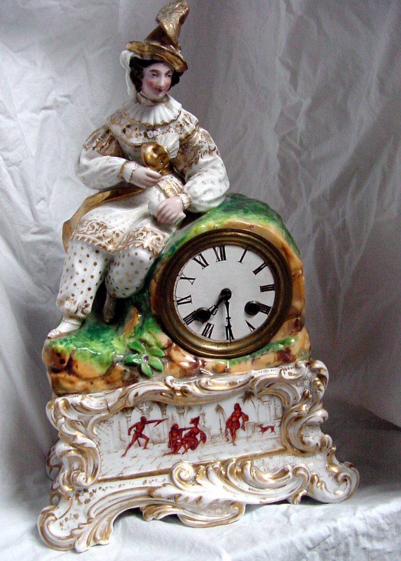 19th Cent. French Mantle Clock: Unsigned but either Old Paris or early 19th Cent. Staffordshire, reclining figure holding a harlequin mask in right hand and glove in left, feather on hat, the front of the clock has leaves molded and