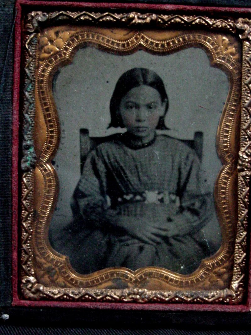 Tintype of a Seated Child, Possible Mixed Indian: Found with the above Indian lady in the same trunk in Morristown, Tennessee, no identification for either, the child is seated in a ladder back chair with folded hands and some sort of decorative belt