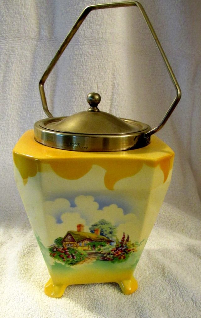 English Cracker Jar w/Thatched Roof Design: Made in England, Hanley, L & Sons, Ltd., cream colored background with floral designs in front of a half timbered house and thatched roof, 5" wide, 10" tall to the top of the handle.