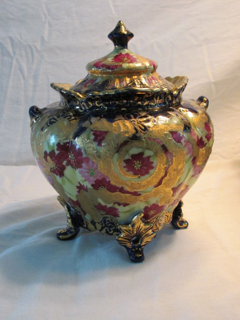 Nippon Covered Footed Urn: Heavily gold trimmed with textured designs over pink and red flowers, cobalt blue trim, old oriental marking on the base, 4 applied feet with gold trimmed designs, small handles ribbed or paneled side
