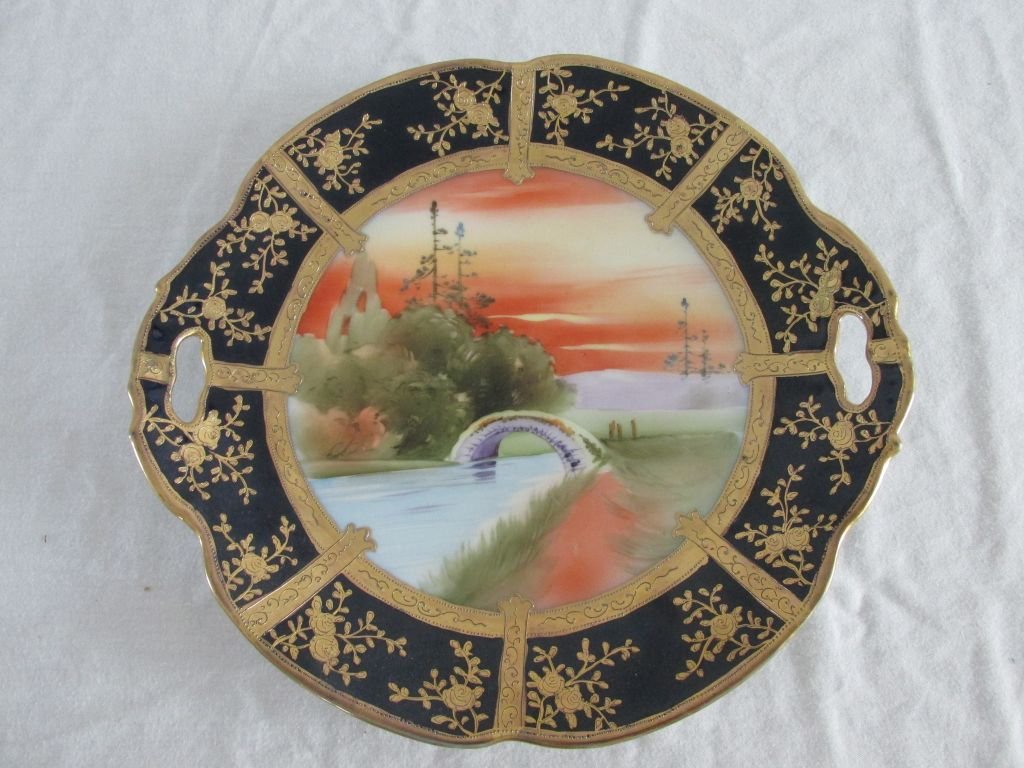 Nippon Scenic Cake Plate: Wide cobalt border with heavy gold painting, center image of a curved bridge over a stream with trees in the background and an orange sky. Open pierced handles, all hand painted and marked on the back