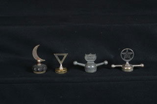 ASSORTED RADIATOR CAPS Lot includes a Ford Model: Lot includes a Ford Model T baby Lincoln dog bone radiator cap; a Star Car circle on dog bone radiator cap; a 1915 Hudson triangle radiator cap; and a 1912-28 Moon radiator cap.