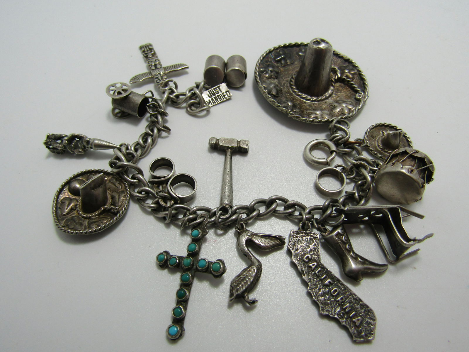 TURQUOISE STERLING SOUTHWESTERN CHARM BRACELET: 16 TOTAL CHARMS. TURQUOISE CROSS, SNARE DRUM, SOMBREROS, CALIFORNIA, PELICAN, CHAIR, BOOT, GNOME, TOTEM POLE, AND OTHERS. WEIGHS 37 GRAMS, MEASURES 7" LONG. LARGEST CHARM IS 1-3/8". USA SHIPPING $5.