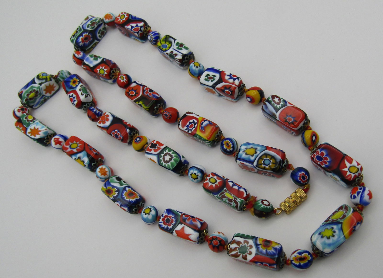 28" MURANO MILLEFIORE NECKLACE ART GLASS VENETIAN: BEAUTIFUL MID CENTURY VINTAGE ESTATE 28 INCH LONG ITALIAN HANDMADE GLASS BEAD NECKLACE. BLOCK BEADS 18MM BY 10MM AND ROUND 8MM. EACH BEAD KNOTTED WITH METAL SPACERS. WEIGHS 108.8 GRAMS. EXCELLENT COND