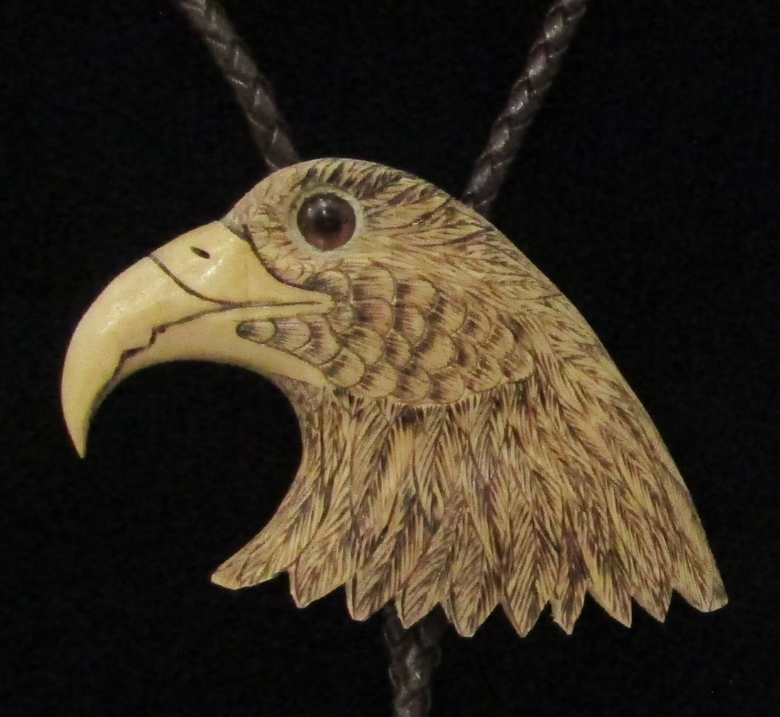 "ROACH" CARVED WOOD EAGLE BOLO TIE NECKLACE: ARTIST SIGNED "???BUD ROACH"; VERY DETAILED VINTAGE ESTATE EAGLE BOLO MEASURES 3 INCHES BY 2 INCHES. 36 INCH LONG NECKLACE. EXCELLENT CONDITION. WITH IMPERIAL AUCTION THE COST FOR PACKING AND SHIPPING