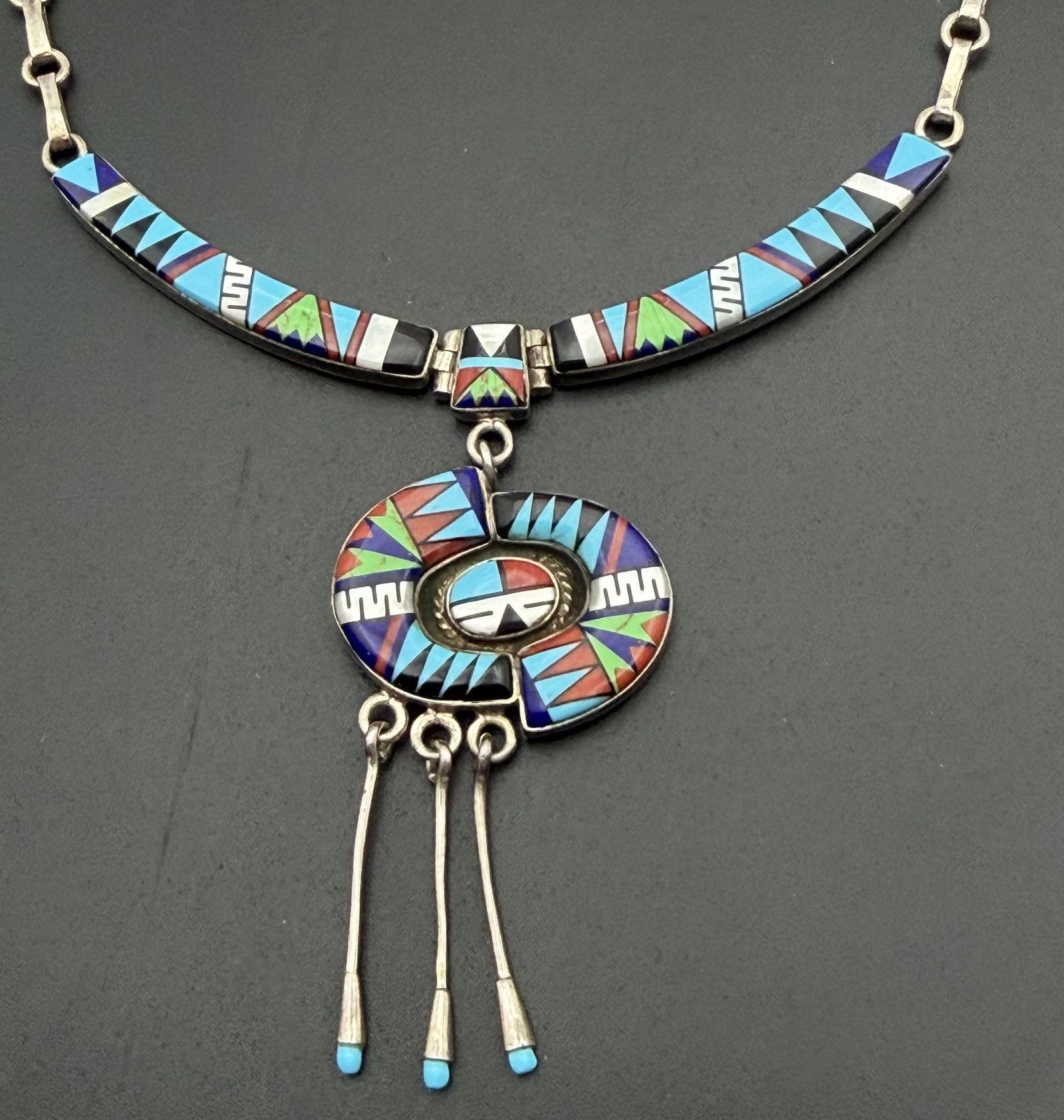 "EJ" STERLING SUNFACE INLAID TURQUOISE NECKLACE: NATIVE AMERICAN HANDMADE INLAID MULTICOLOR STONE NECKLACE. SIMULATED TURQUOISE MOTHER OF PEARL ONYX GASPEITE LAPIS AND SHELL. SIGNED "EJ" TESTED STERLING SILVER. MEASURES 21.5". CENTER SECTION IS 3.5"