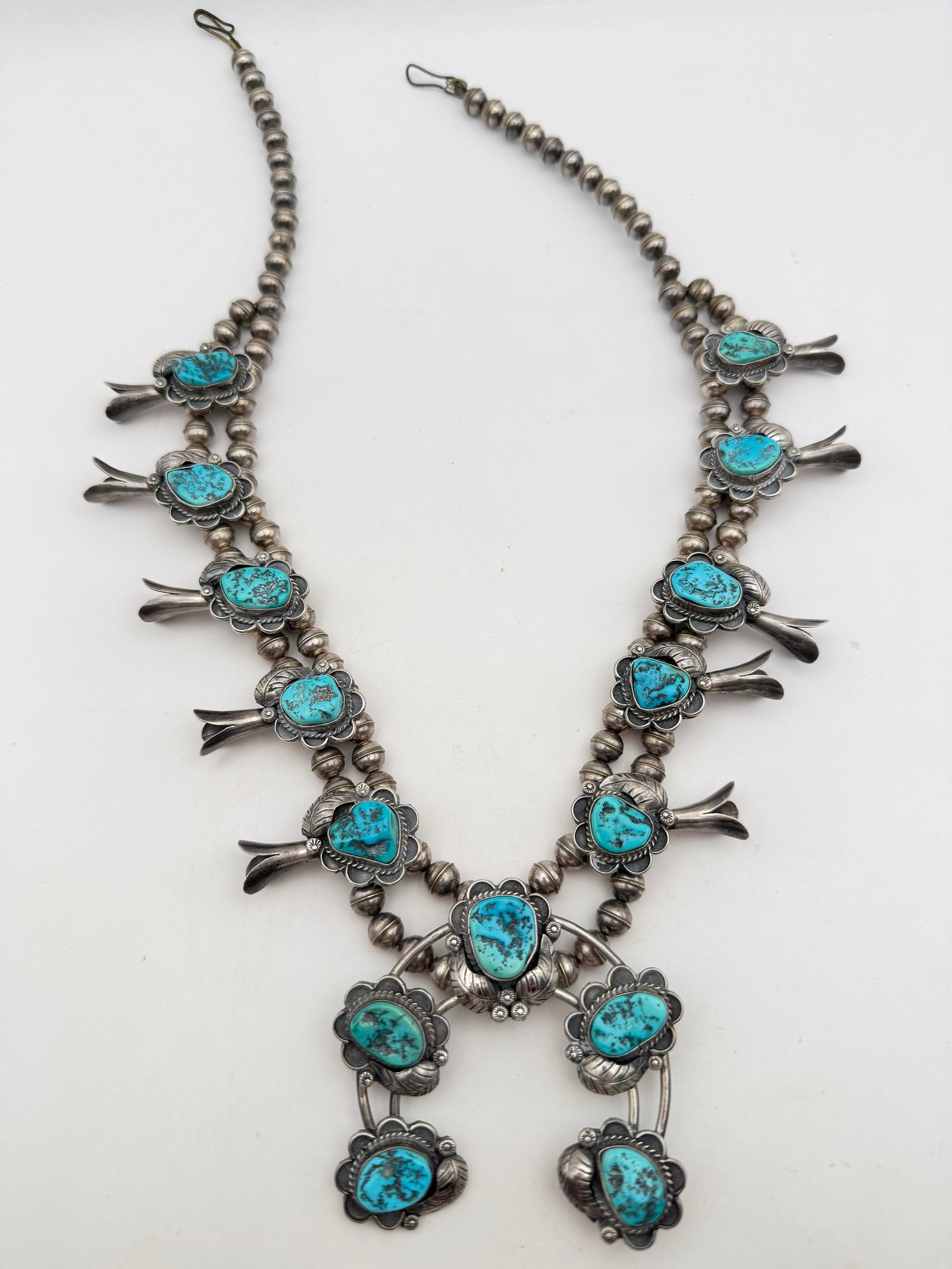STERLING NAVAJO TURQUOISE SQUASH BLOSSOM NECKLACE: VINTAGE OLD PAWN 1980'S NATIVE AMERICAN NAVAJO HANDMADE NECKLACE. HIGH QUALITY CRAFTSMANSHIP. POSSIBLY SIGNED "XI" OR "KI" WITH SCRATCHES. NO METAL PURITY MARK, TESTED STERLING SILVER. MEASURES 23". N