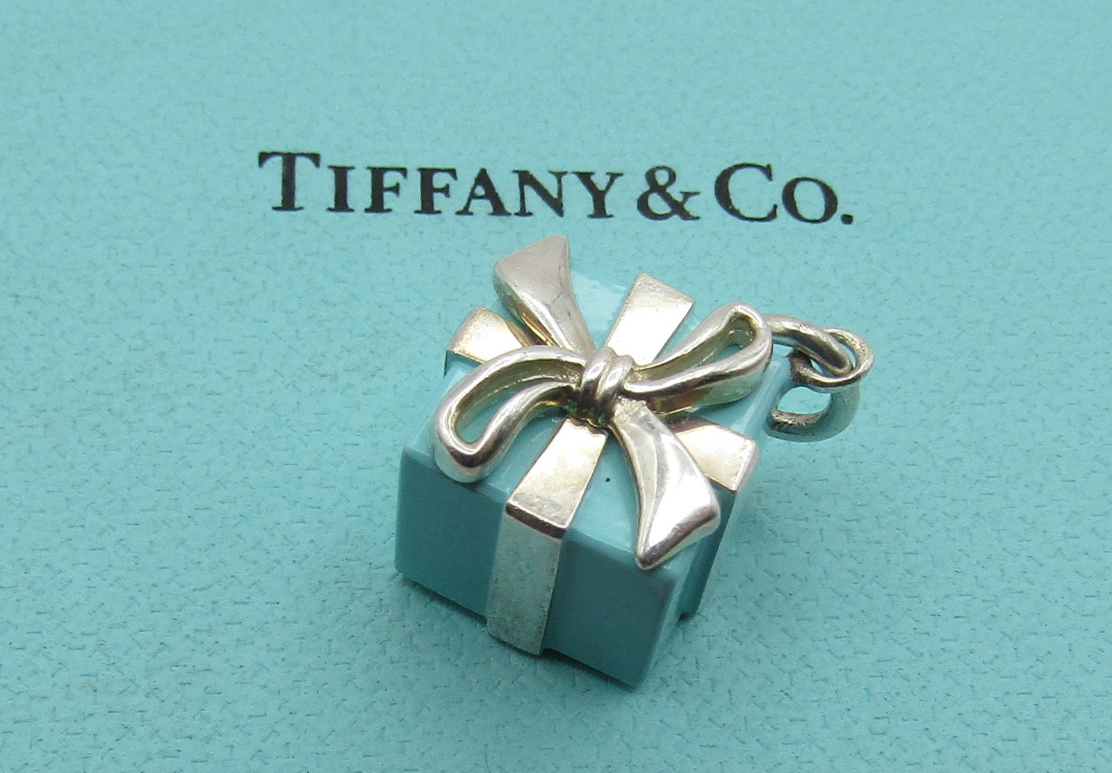 TIFFANY & CO BLUE GIFT BOX CHARM STERLING SILVER: GENUINE SIGNED "T & CO. 925" WITH POUCH. MEASURES 1/2 INCH BY 1/2" BY 1/2". WEIGHS 7.8GRAMS STERLING SILVER. EXCELLENT USED CONDITION. WITH IMPERIAL AUCTION THE COST FOR PACKING AND SHIPPING VIA USPS 