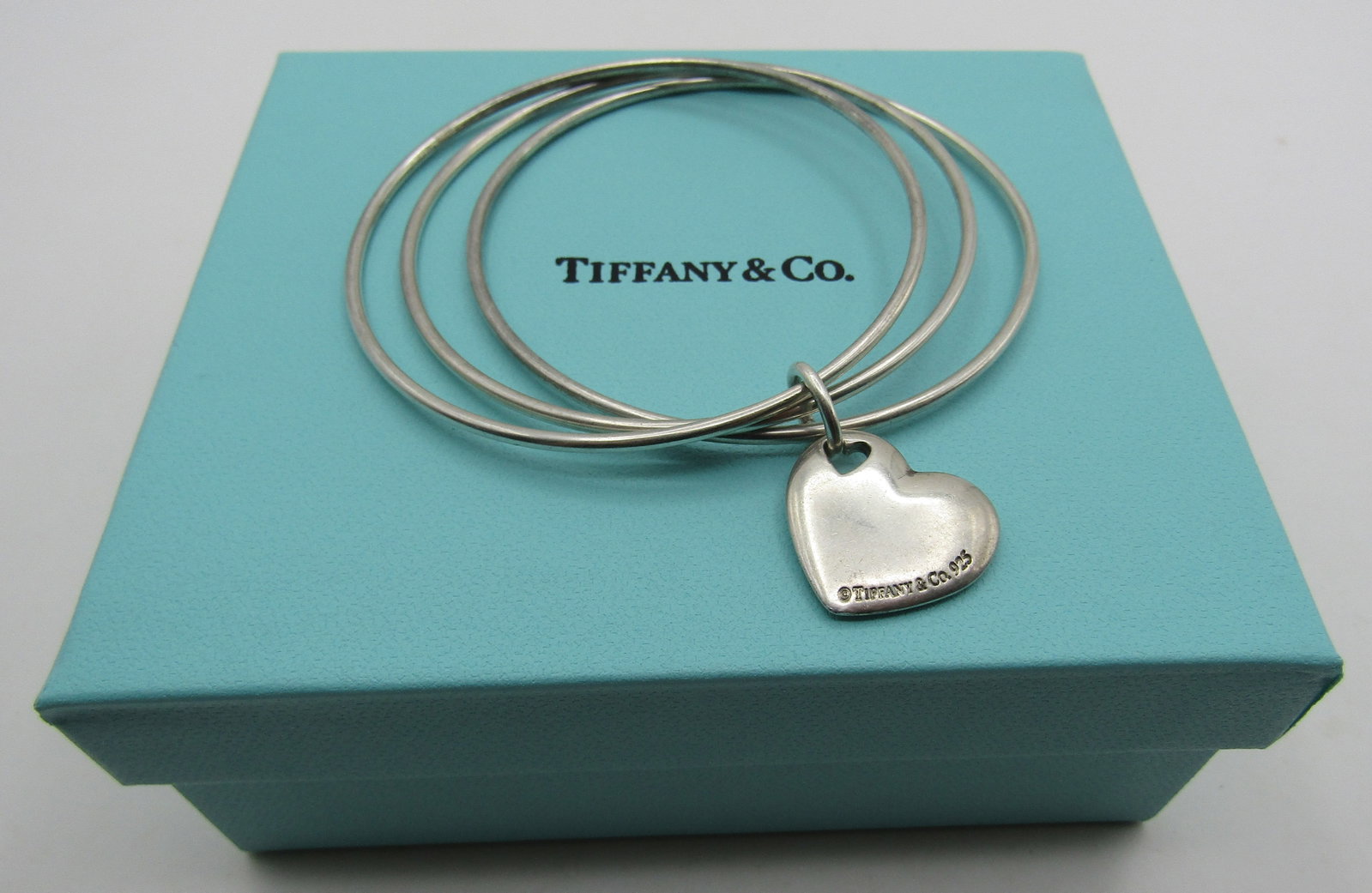 TIFFANY & CO HEART 3 BANGLE BRACELET STERLING SILV: GENUINE SIGNED "TIFFANY & CO. 925" HEART WITH 3 BANGLE BRACELETS; WITH TIFFANY BOX. WEIGHS 23.8 GRAMS STERLING SILVER. EXCELLENT USED CONDITION. WITH IMPERIAL AUCTION THE COST FOR PACKING AND SHIPPING