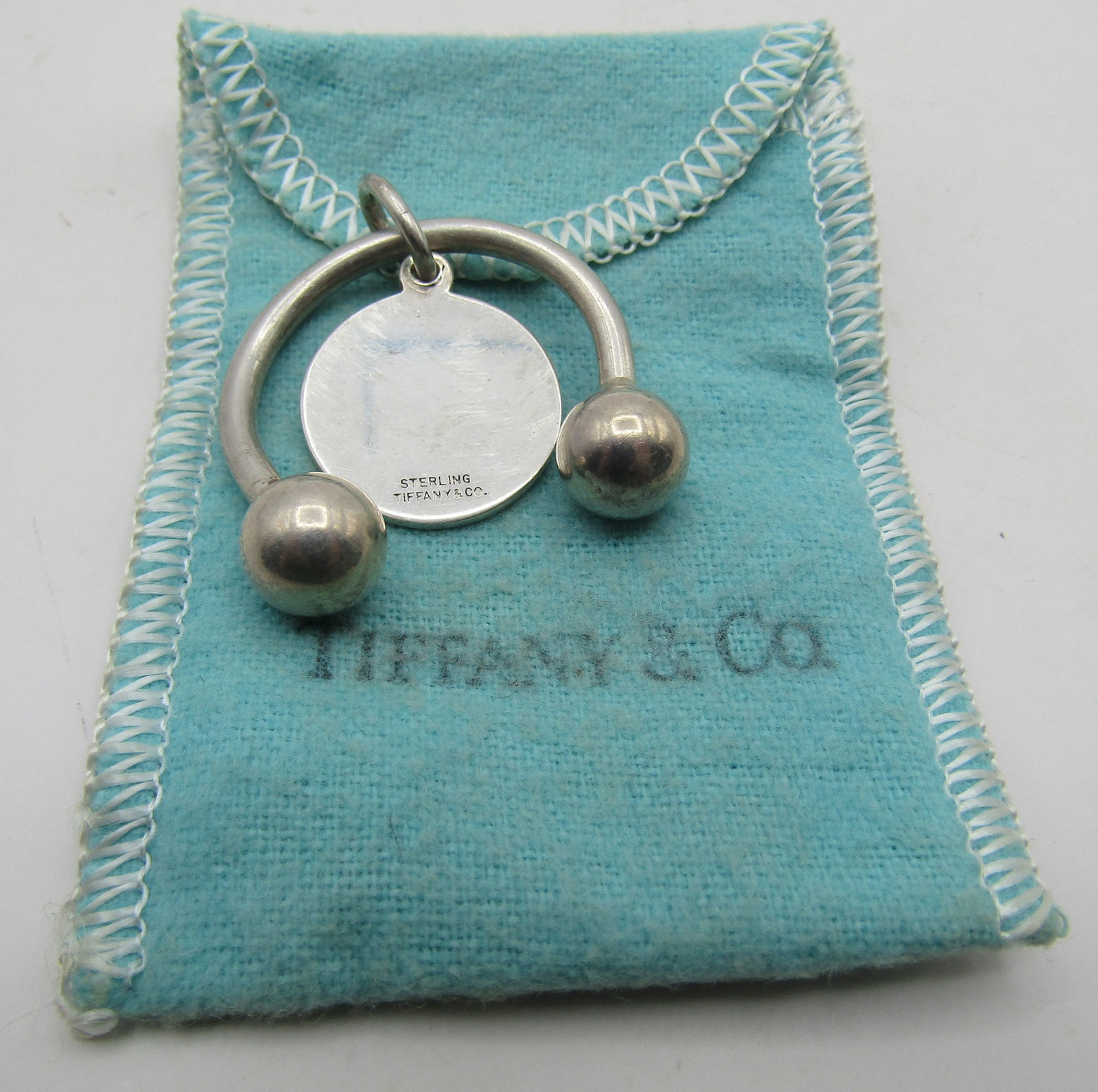 TIFFANY & CO TAG WITH KEYRING STERLING SILVER 10GR: GENUINE SIGNED "TIFFANY & CO. STERLING" TAG WITH KEYRING WITH POUCH. MEASURES 2.5 INCHES LONG. WEIGHS 10.0 GRAMS STERLING SILVER. EXCELLENT USED CONDITION. WITH IMPERIAL AUCTION THE COST FOR PACKING A