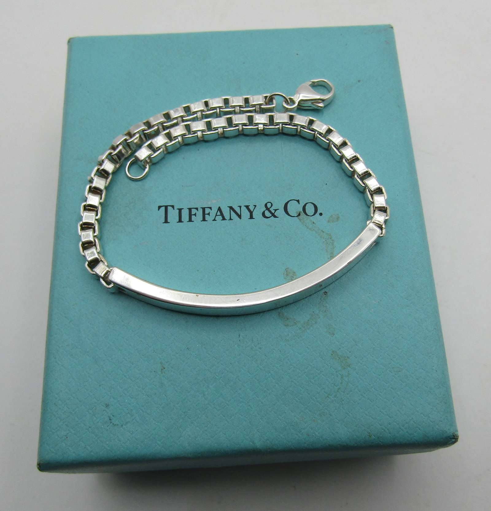 TIFFANY & CO BOX LINK ID BRACELET STERLING SILVER: GENUINE SIGNED "TIFFANY & CO. AG, 925" WITH BOX. LINK CHAIN MEASURES 8.5 INCHES LONG. WEIGHS 21.3 GRAMS STERLING SILVER. EXCELLENT USED CONDITION. WITH IMPERIAL AUCTION THE COST FOR PACKING AND SHIPPI