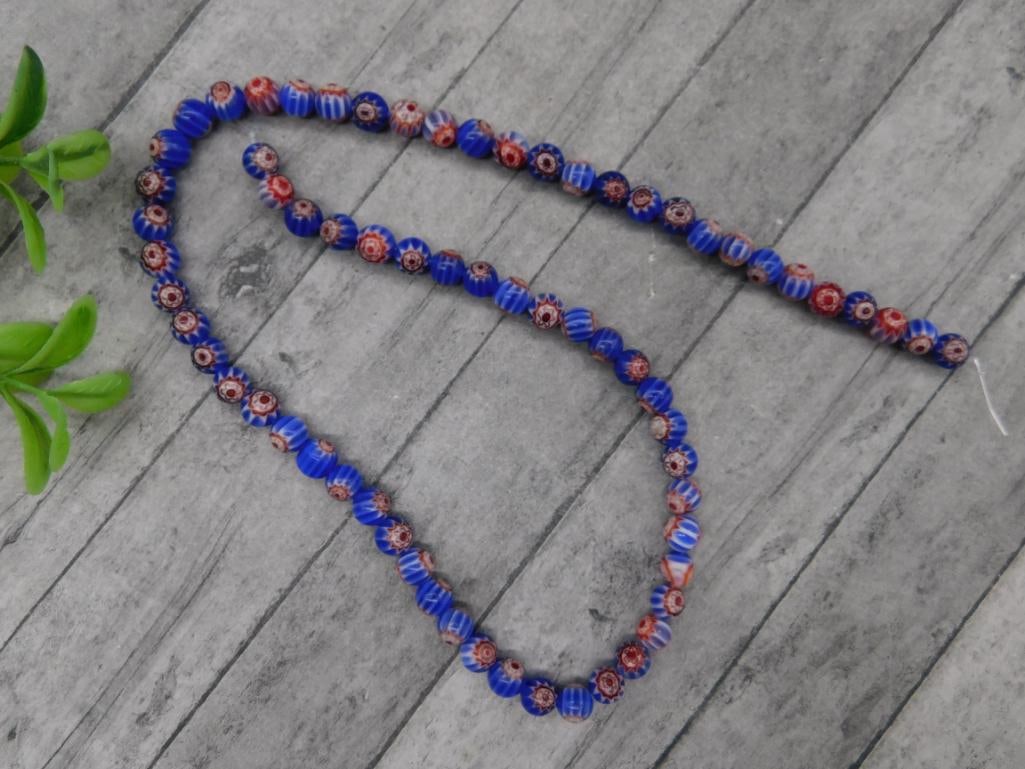 African Trade Beads: A strand of blue and red trade beads featuring a floral-like pattern. Each bead is individually handcrafted with intricate detailing. The strand measures approximately 19 inches in length with a total