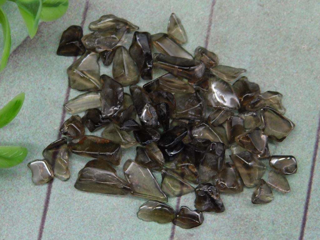12 Grams of Smokey Quartz Crystals: Lot of 12 grams of smokey quartz crystals. Includes numerous small crystal pieces with a dark, smoky hue. Ideal for collectors, jewelry-making, and other craft projects. See reference coin for a sense