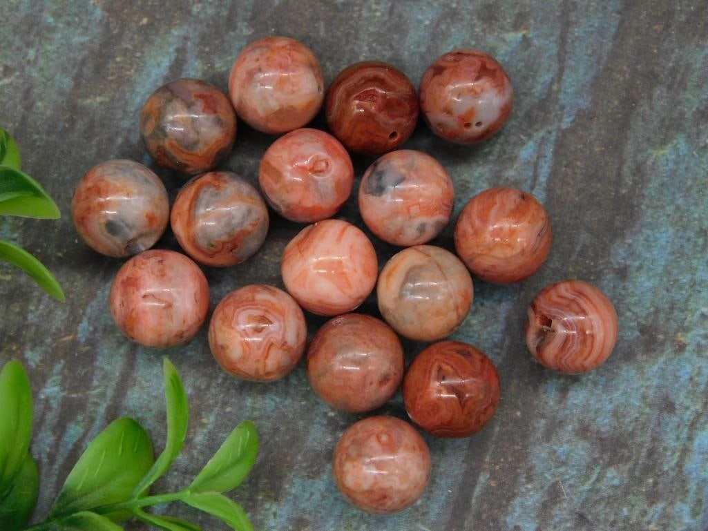 Lot of Polished Red Banded Agate Beads: This is a lot of 16 polished red banded agate beads weighing approximately 42 grams in total. These spherical beads feature unique natural patterns and variations in shades of red, pink, and gray. Eac