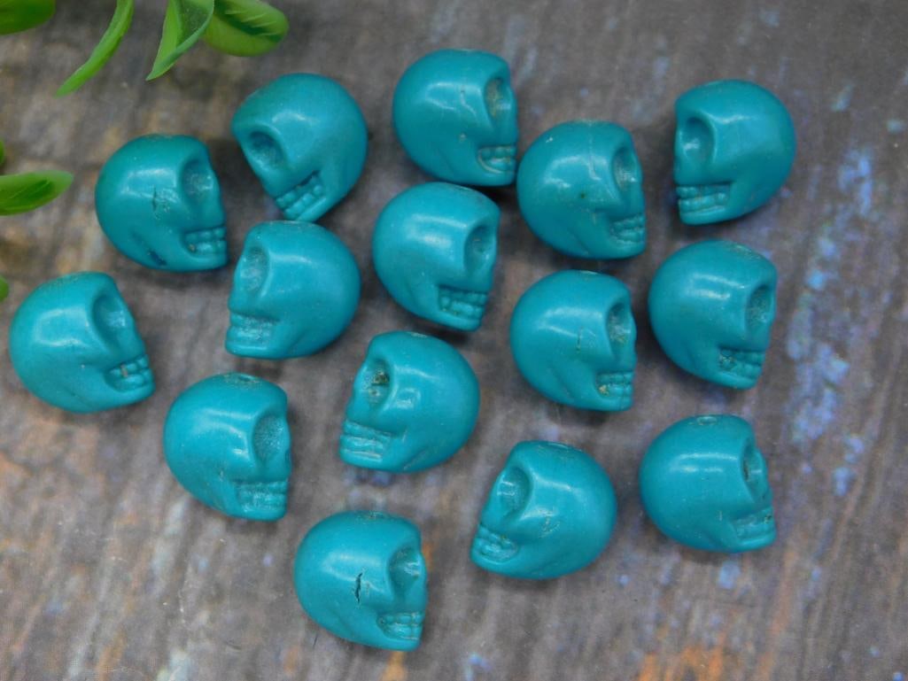 Set of 15 Miniature Turquoise Skull Beads: A collection of 15 miniature turquoise-colored skull beads. Each bead features sculpted detailing and is lightweight. Combined weight totals 32 grams. Ideal for crafting or jewelry-making projects.