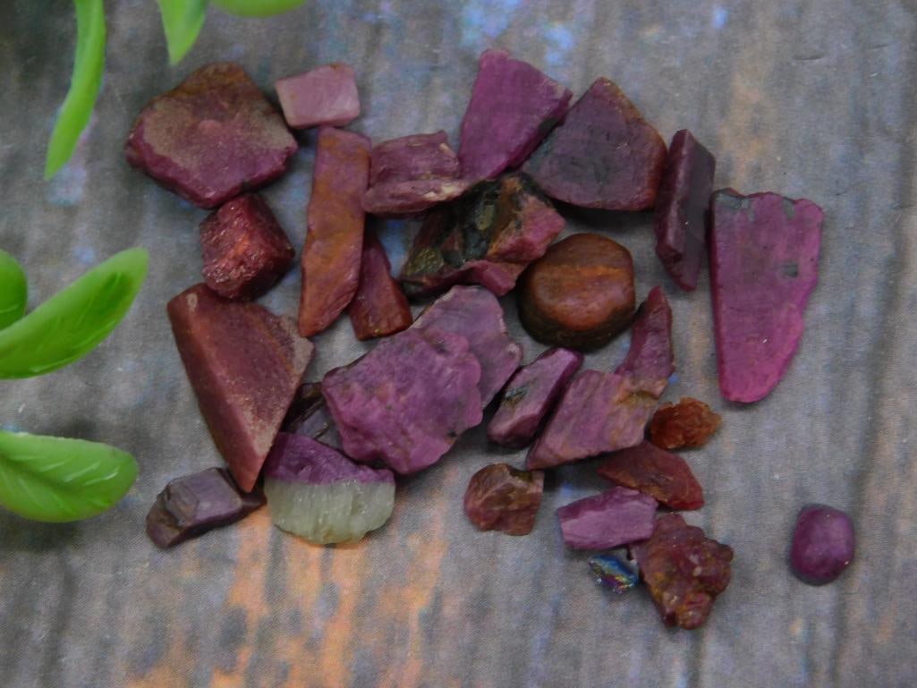Mixed Lot of Raw Purplish Stones: Mixed collection of raw stones in shades of purplish hues. Includes various shapes and sizes. The listed weight is approximately 12 grams. A U.S. quarter shown for size reference. Ideal for collectors