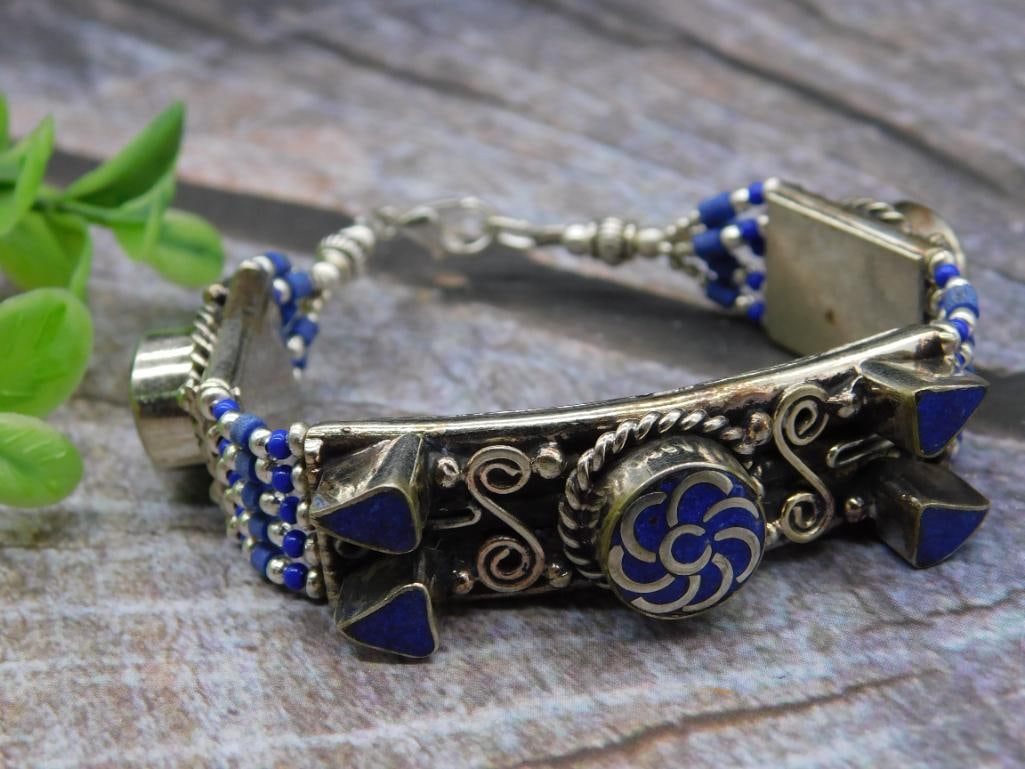 Silver and Beaded Bracelet with Lapis Lazuli Accents: Silver bracelet featuring detailed blue enamel designs and intricate beadwork. Embellished with triangular and floral patterns. Adjustable length with hook fastener. Includes a mix of silver-toned met