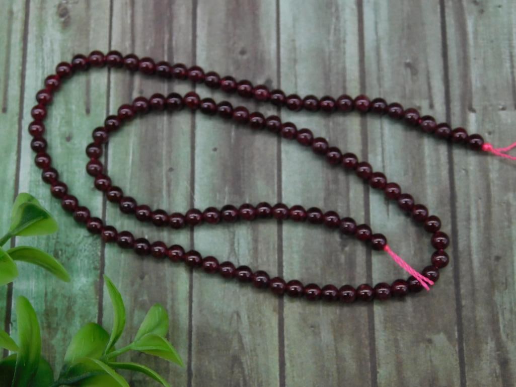 Strand of Small Round Garnet Beads: Full strand of small round garnet beads. Each bead is polished and uniform in size, with a deep reddish color. They are strung together on a pink string. Length of the strand is approximately 16 inche