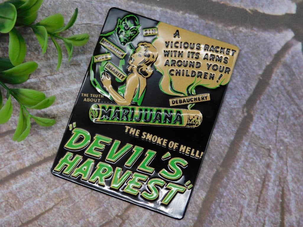 Devil?s Harvest Marijuana Magnet: Colorful tin sign featuring the design for ?Devil?s Harvest? with prominent text and imagery. Measures approximately 3 inches wide, as shown next to a measuring tool. Depicts vintage-style propaganda-